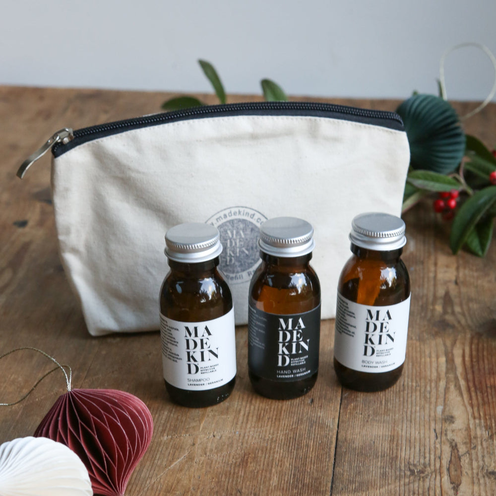 Three bottles of Madekind skincare products with a cream pouch on a wooden surface.