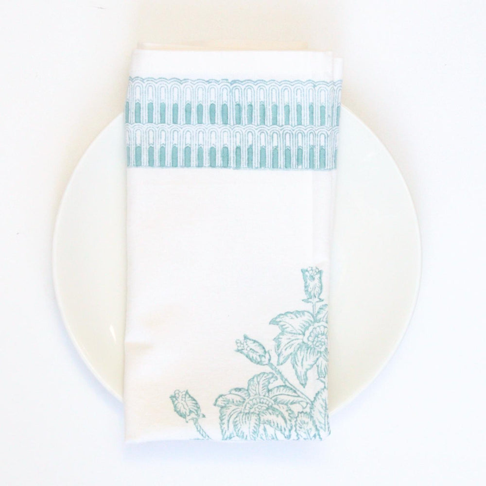 Teal floral patterned napkin on a white plate with a white background