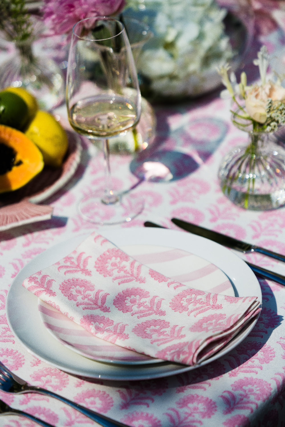 Table setting with pink floral tablecloth, plates, cutlery, and glasses.