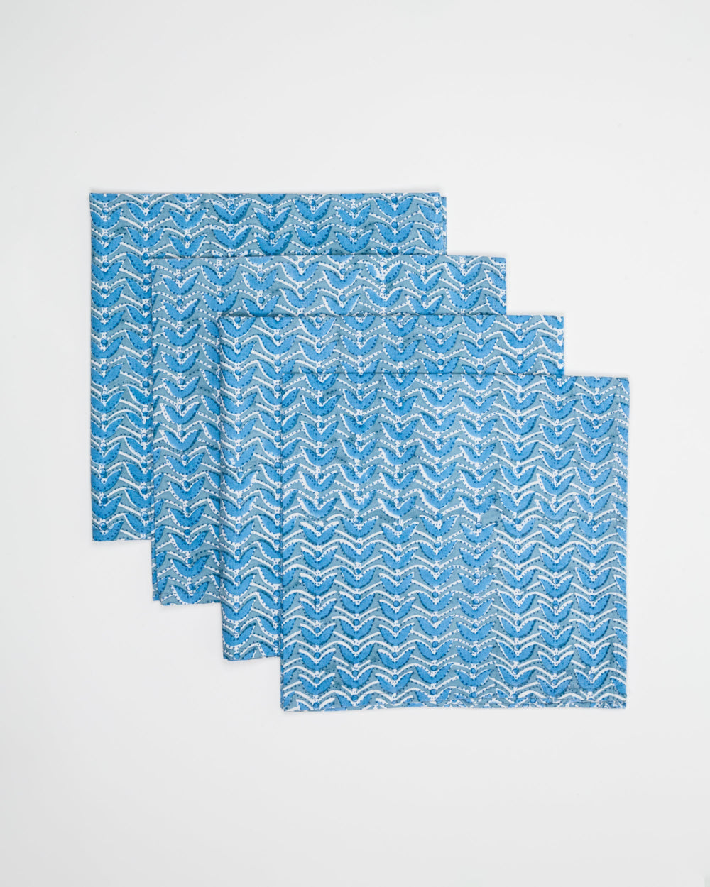 Set of four blue and white patterned napkins on a light grey background