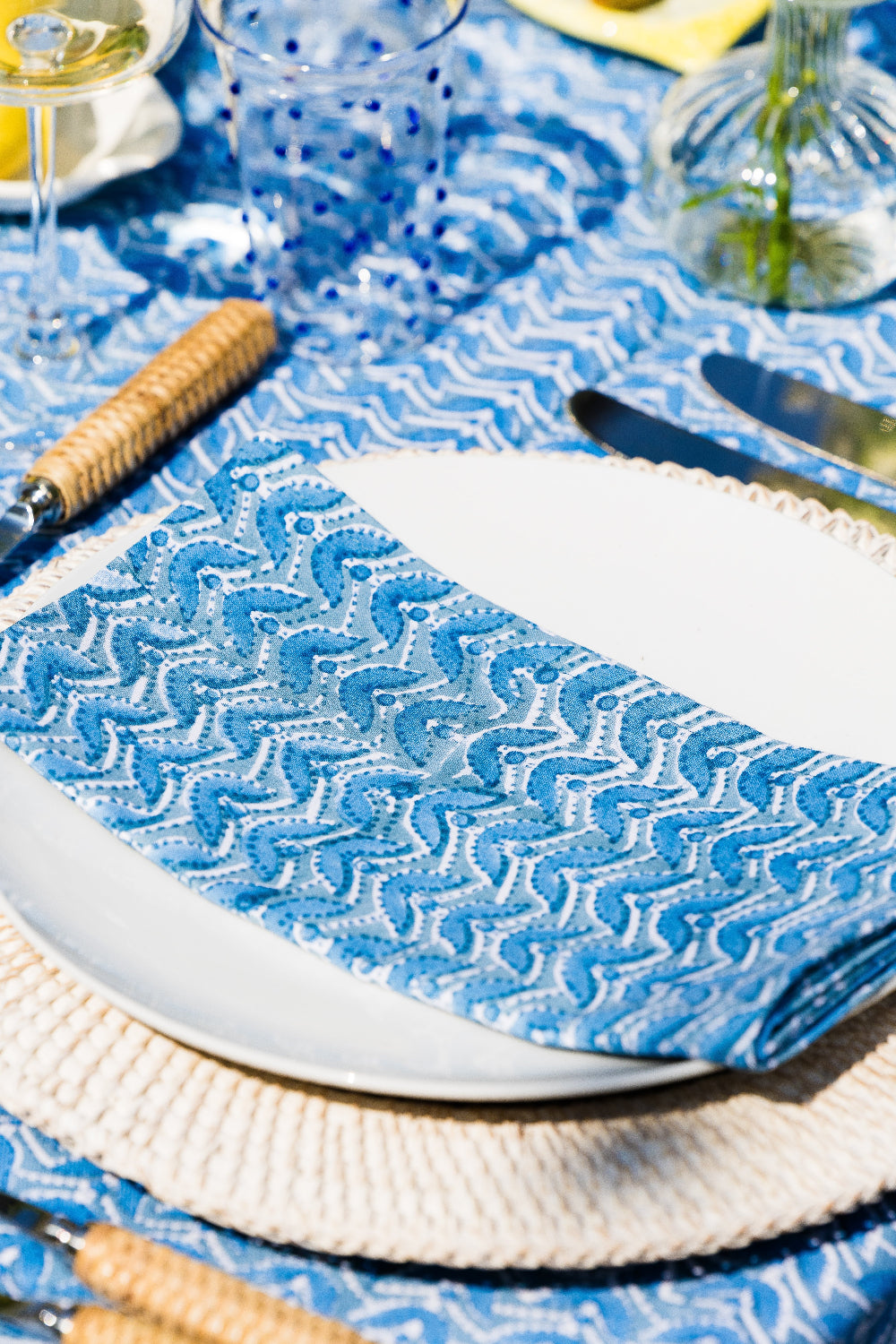 Table setting with blue patterned tablecloth, white plates, and cutlery.