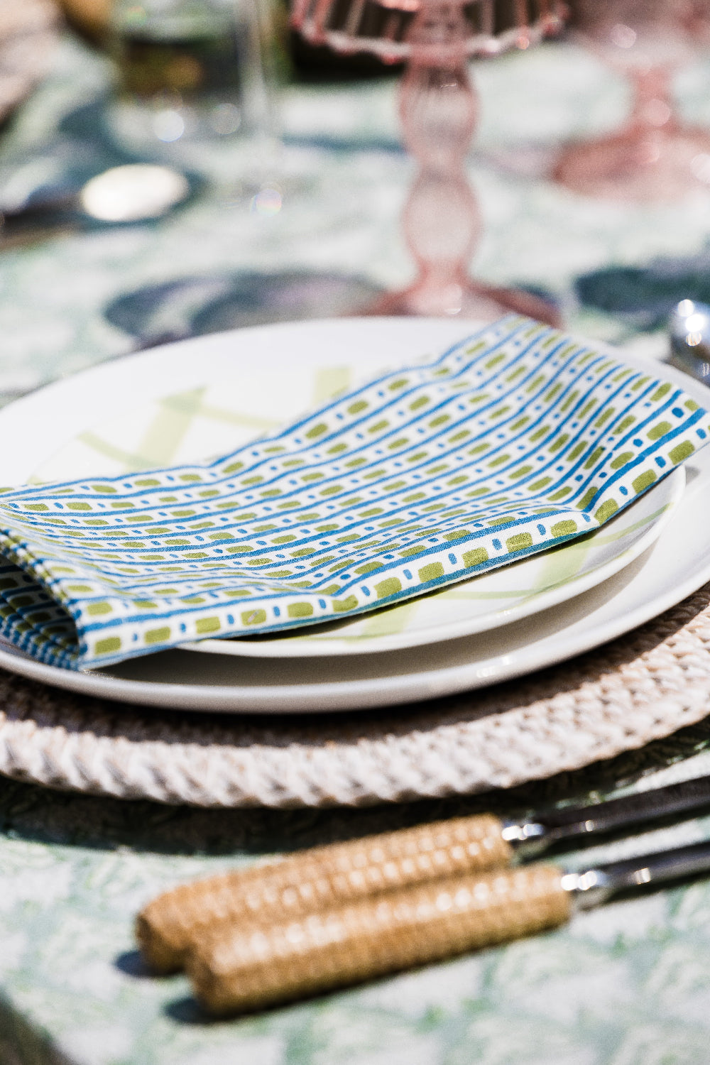 Set table with patterned napkin, plates, and cutlery on a textured surface.