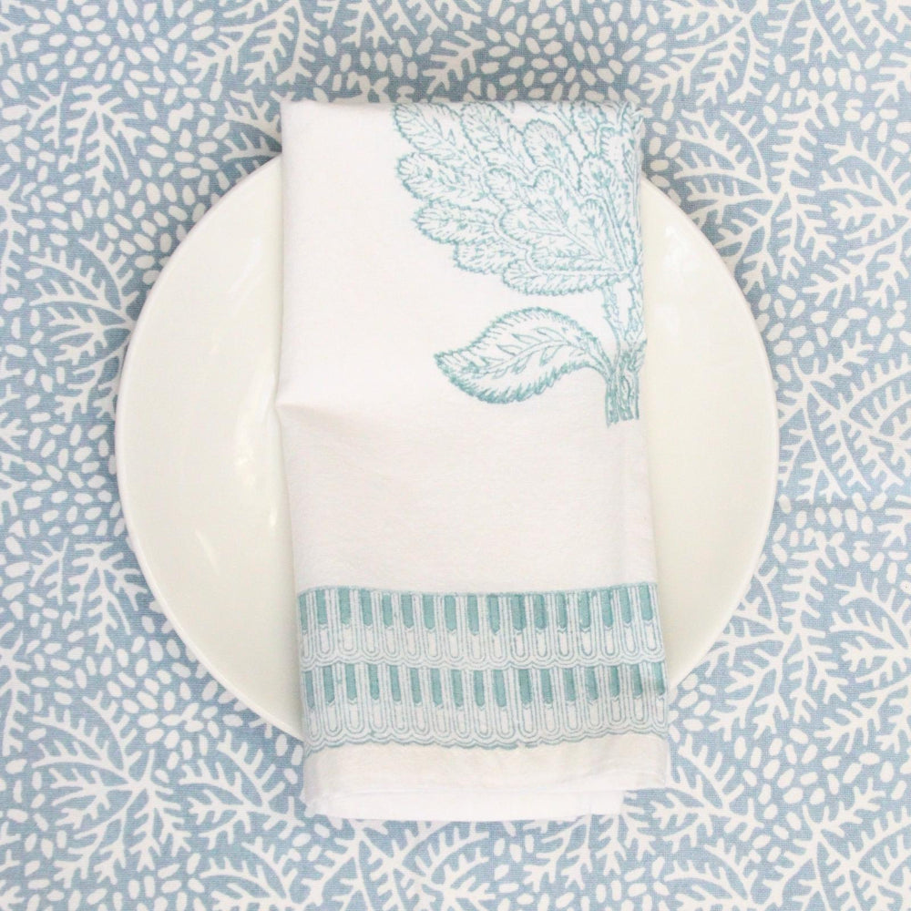 White plate with a folded white napkin featuring blue leaf patterns on a matching blue patterned tablecloth.