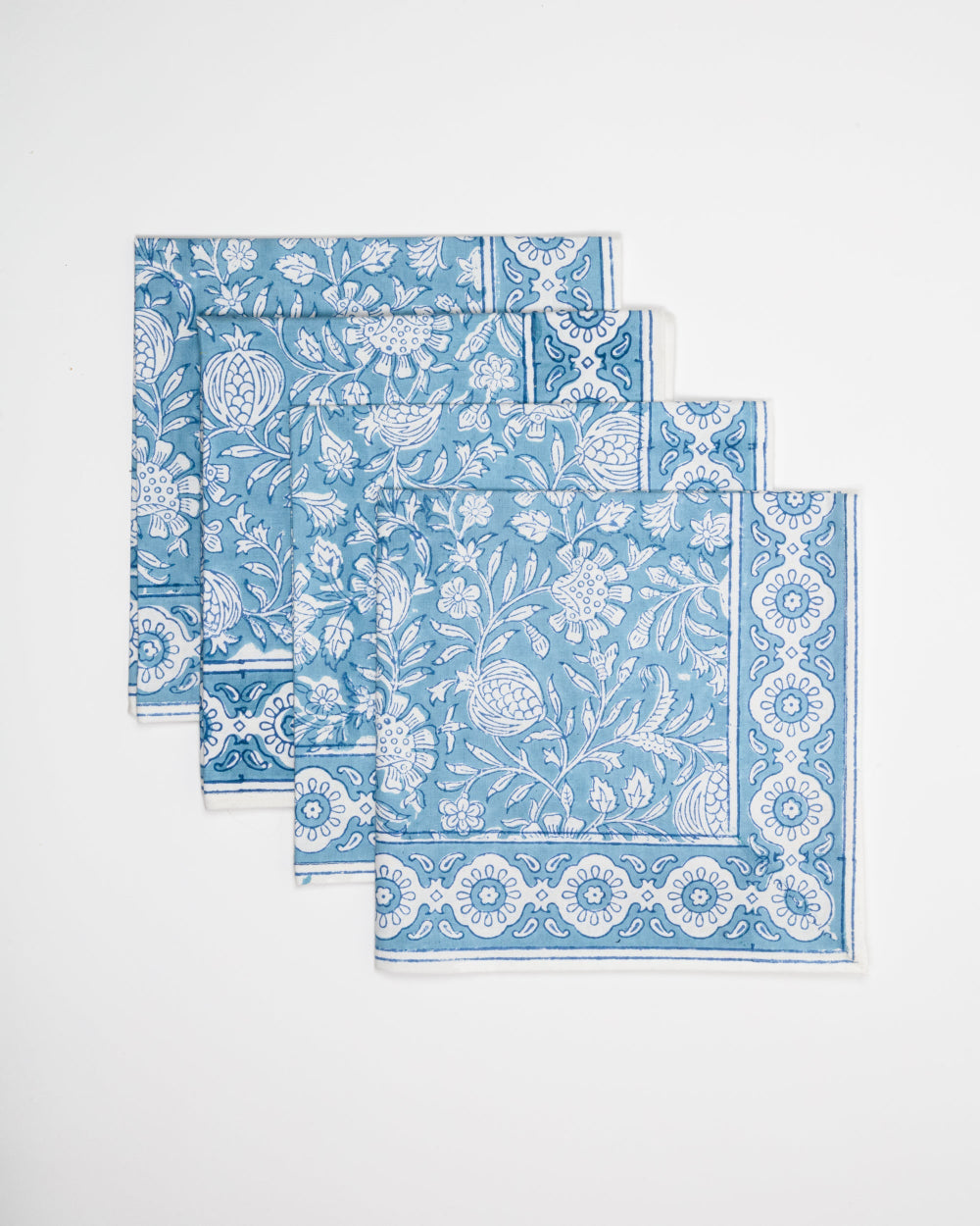 Set of four blue and white patterned napkins on a light grey background
