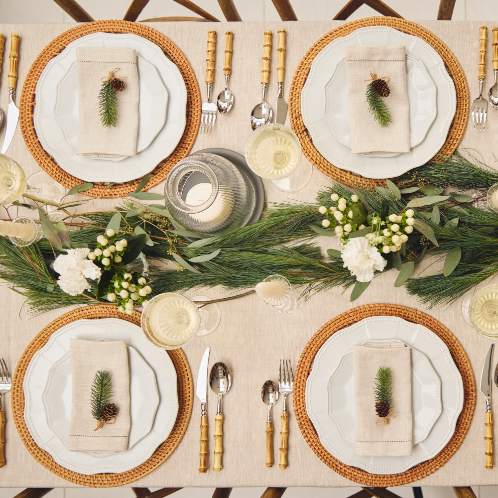 Elegant table setting with woven placemats, white plates, gold cutlery, and greenery.