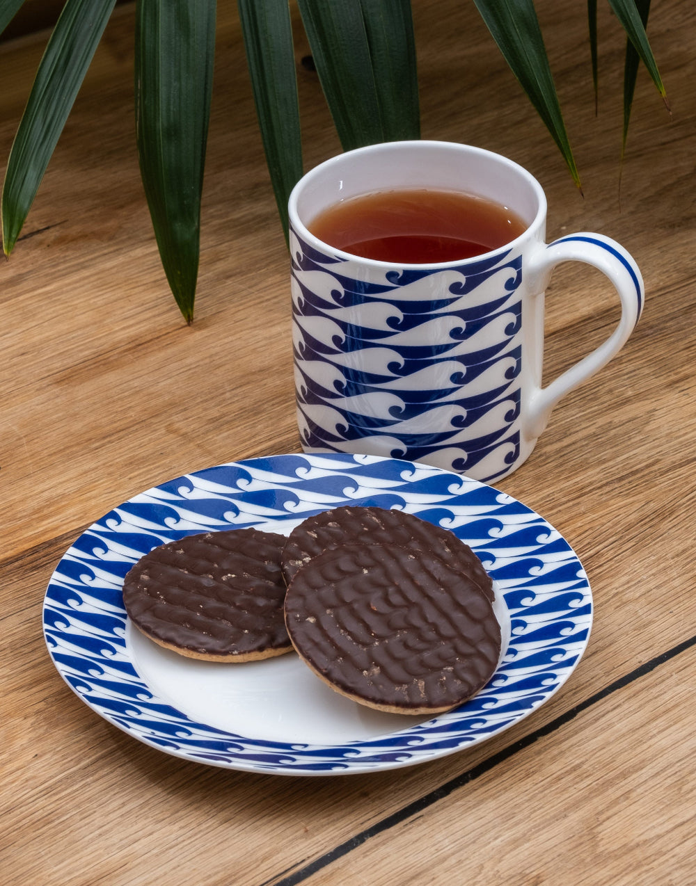 Two chocolate biscuits on a blue and white patterned plate with a matching mug of tea on a wooden surface.