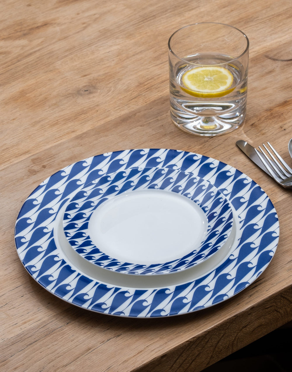 Blue and white patterned plate on a wooden table with a glass of water and slice of lemon.