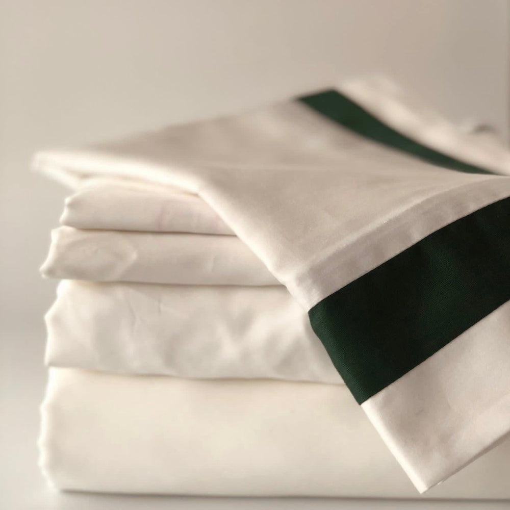 Stack of white Notting Hill bedding with green trim on a light grey background