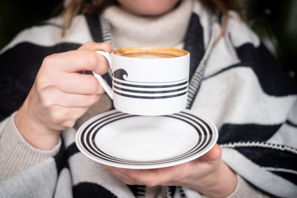 Person holding a striped coffee cup and saucer with a blurred background