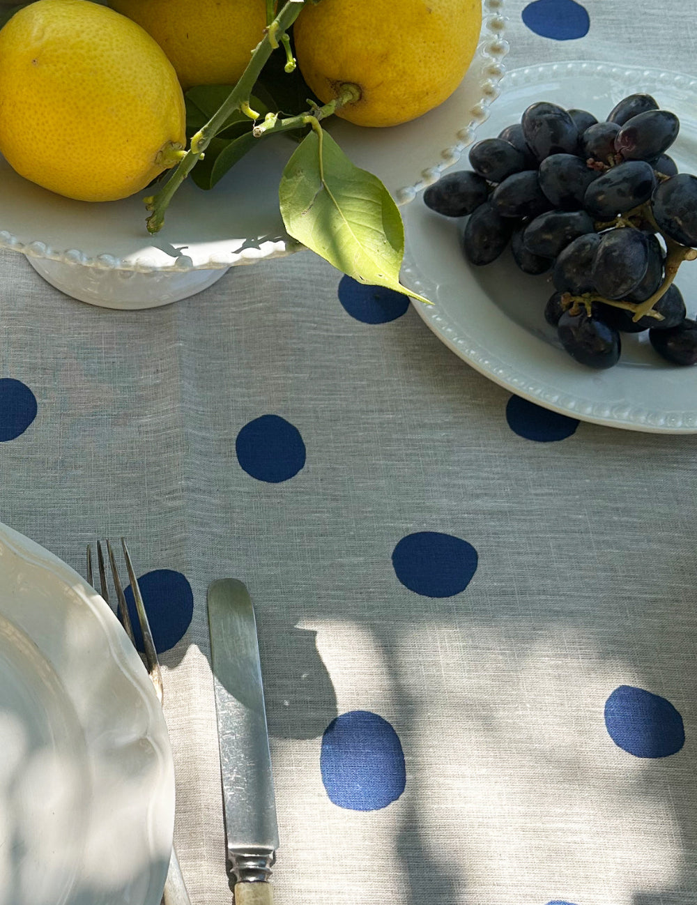 Table setting with lemons, grapes, and cutlery on a polka dot tablecloth.