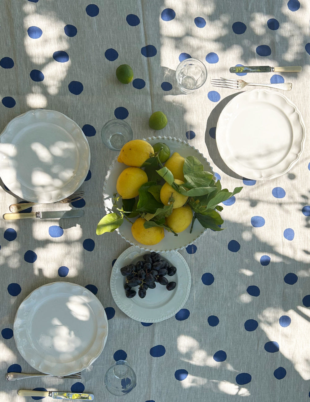 Table setting with lemons, grapes, and a bowl of fruit on a polka dot tablecloth.