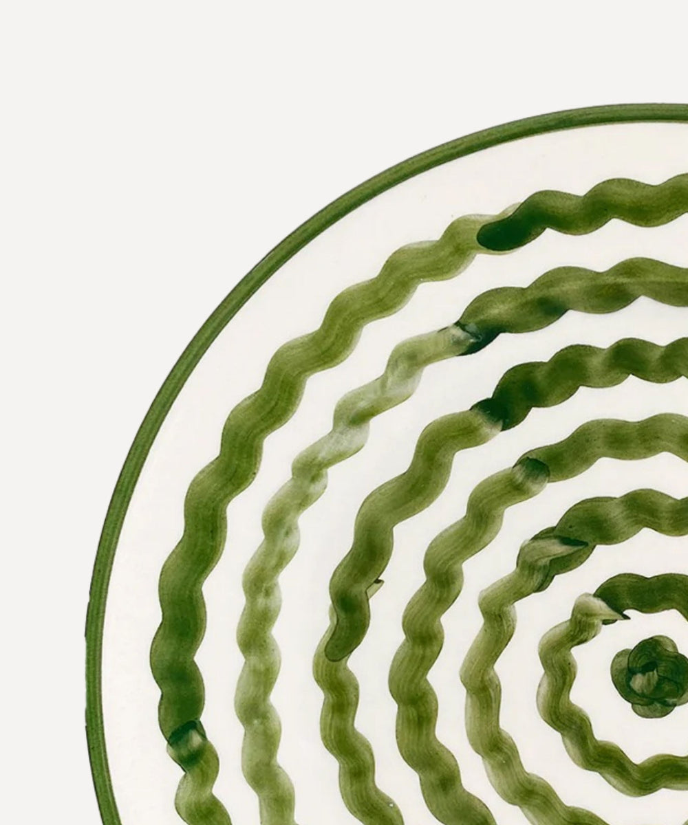 Close-up of a green ceramic plate with wavy pattern on a white background