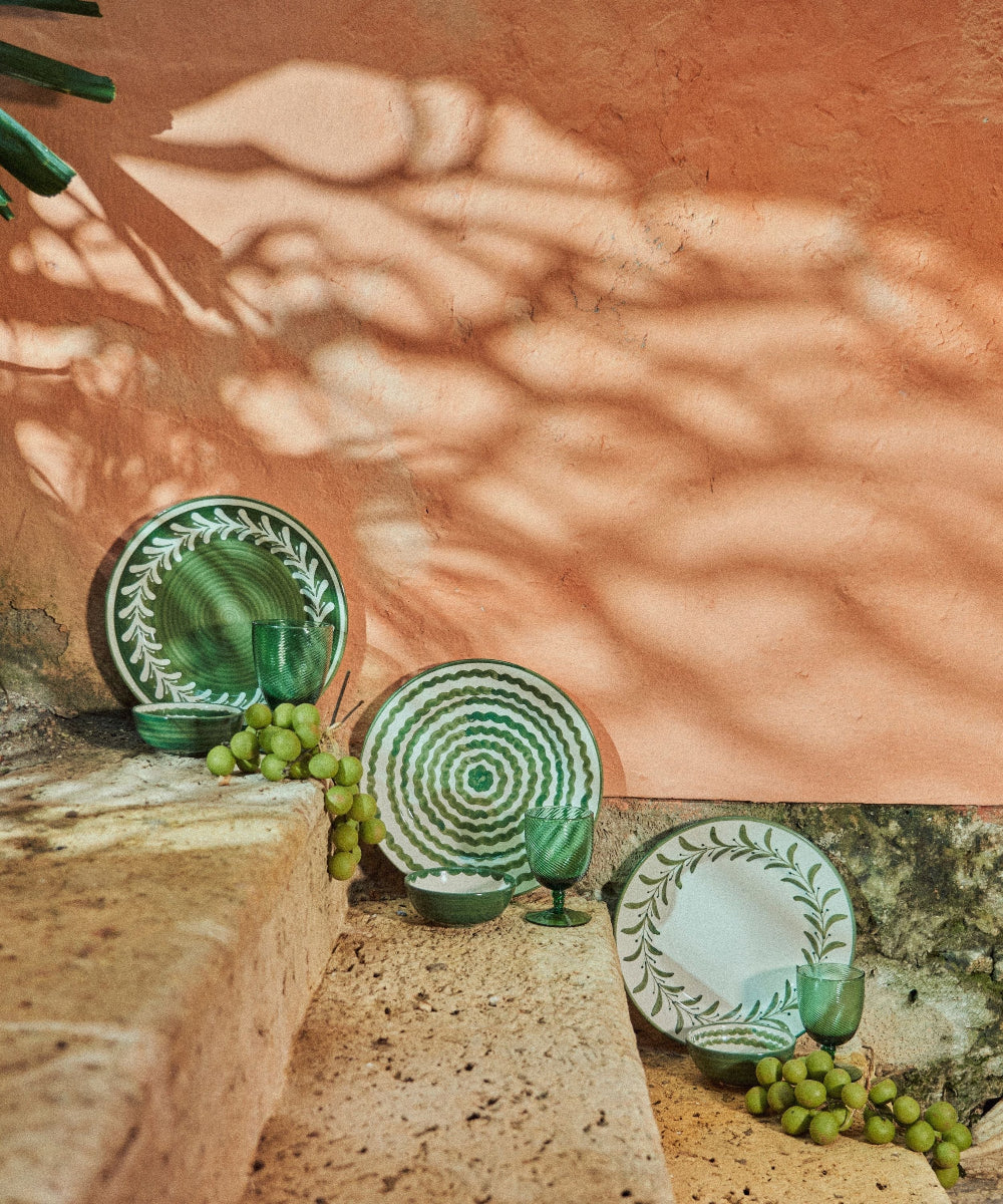 Green ceramic plates and glasses on a stone surface with a textured wall background
