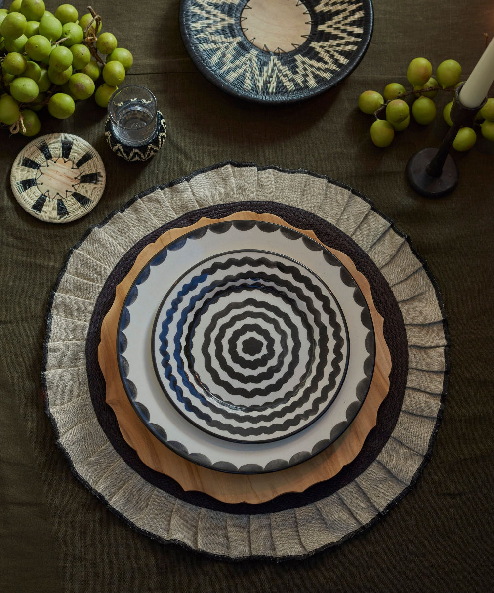 Decorative plate with geometric pattern on a dark surface with grapes and another plate.