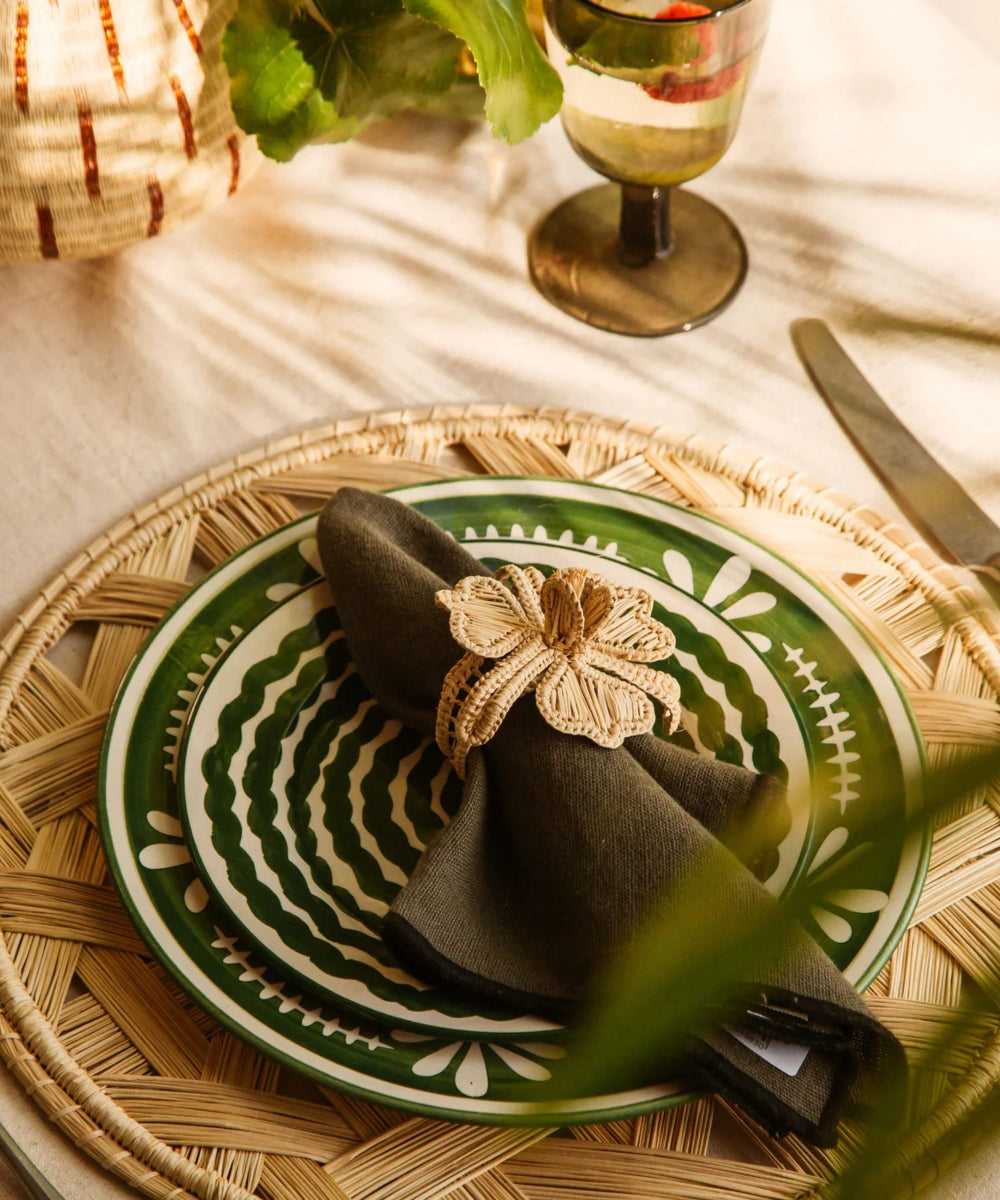 Decorative table setting with a green plate, folded napkin, and decorative napkin ring on a woven placemat.