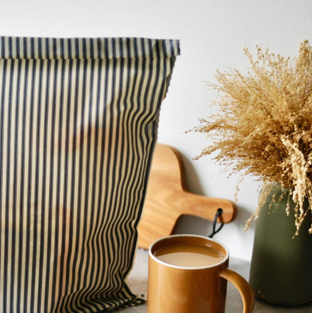 Striped fabric, wooden cutting board, mug with coffee, and dried plant on a white surface