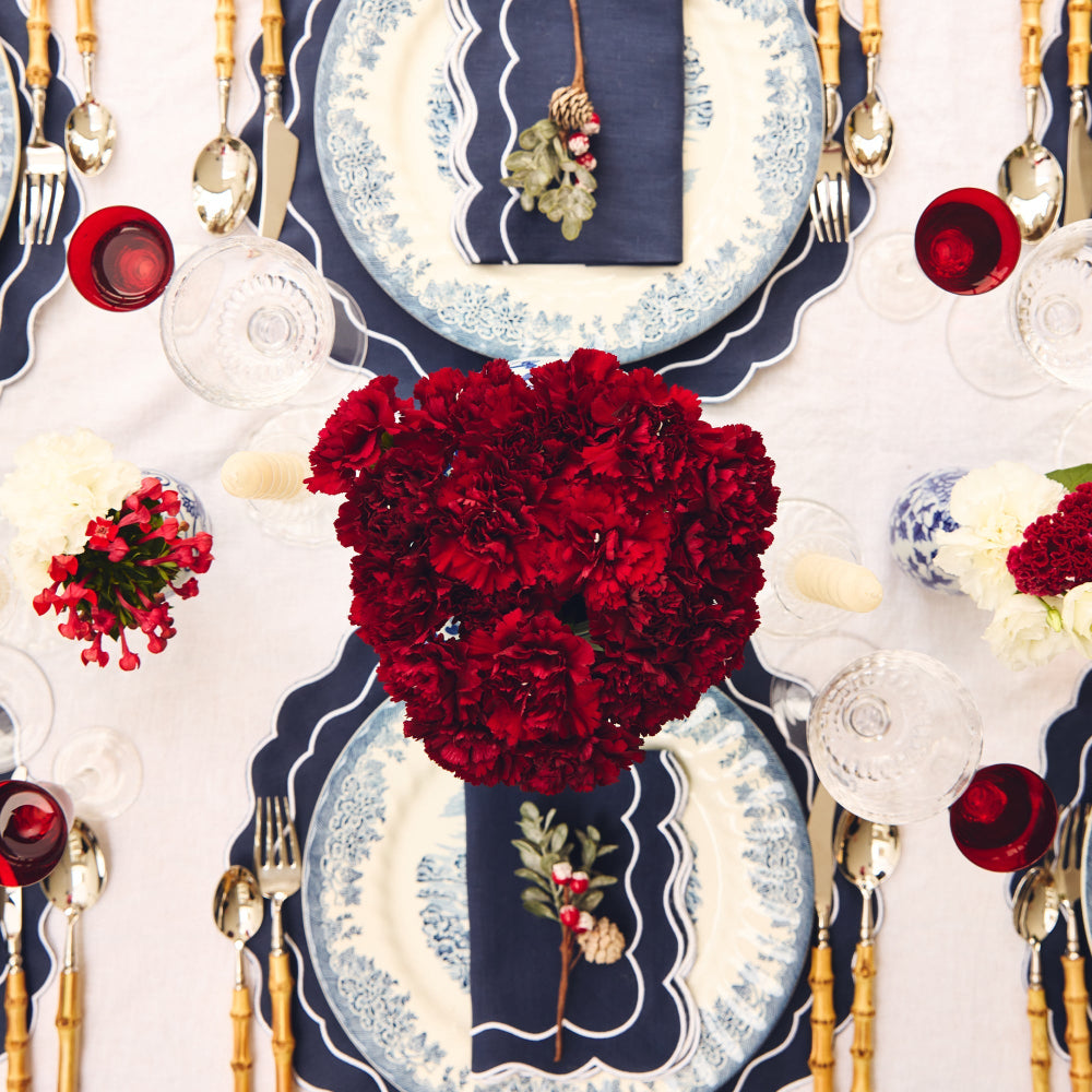 Decorative Christmas table setting with red flowers, blue and white plates, and gold cutlery.