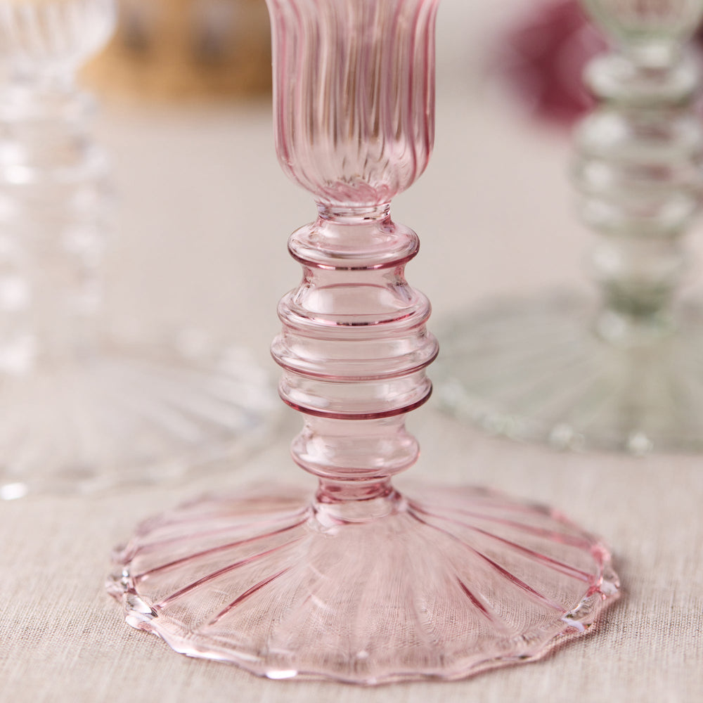 Pink glass candle holder base on a dining table with blurred background