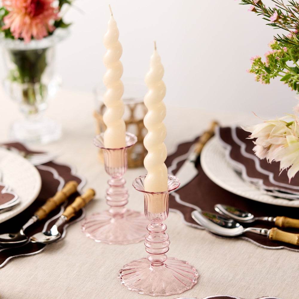 Decorative spiral candles on pink candlesticks with a table setting in the background.