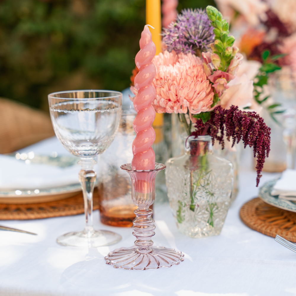 Decorative table setting with a pink candle holder and floral arrangement on a white tablecloth.