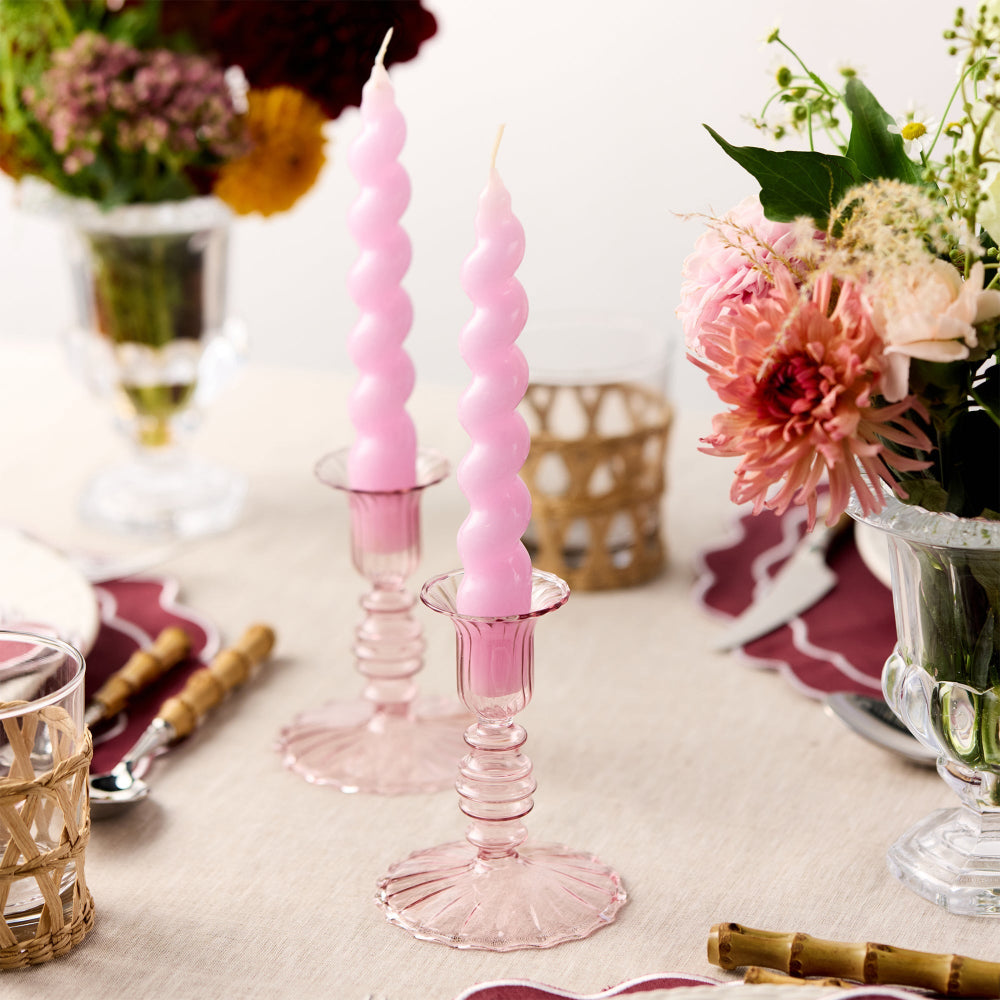 Pink twisted candles in glass holders on a table with floral arrangements and place settings.