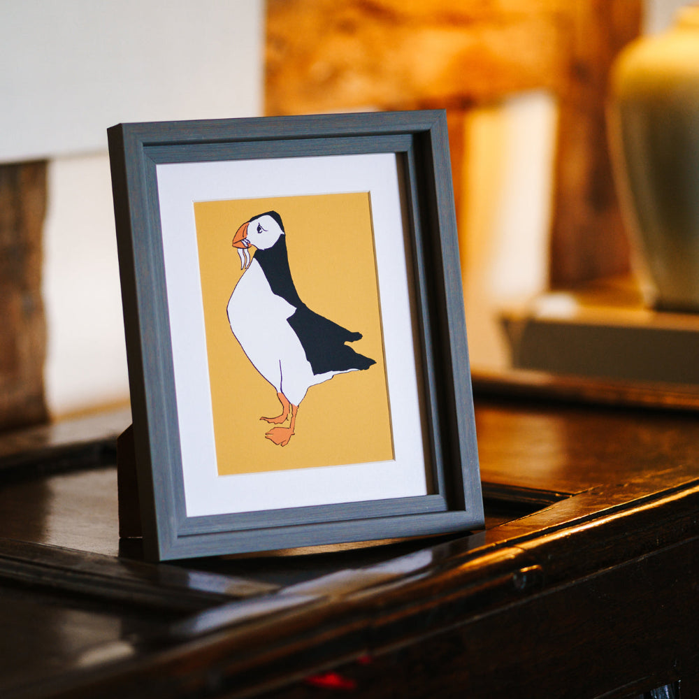 Framed illustration of a puffin on a wooden surface with a blurred background