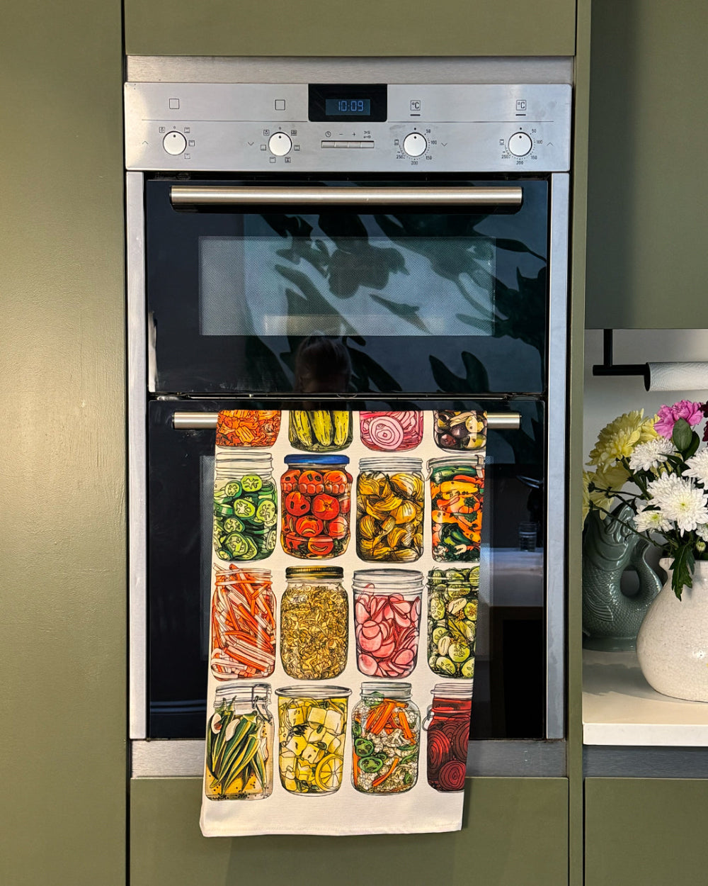 Stainless steel oven with a towel displaying various prepped vegetables hanging on it.