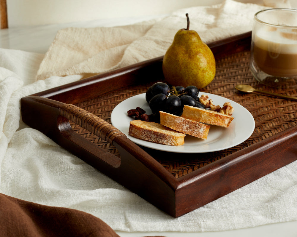 Wooden tray with a plate of food, including a pear, grapes, and bread, on a white surface.