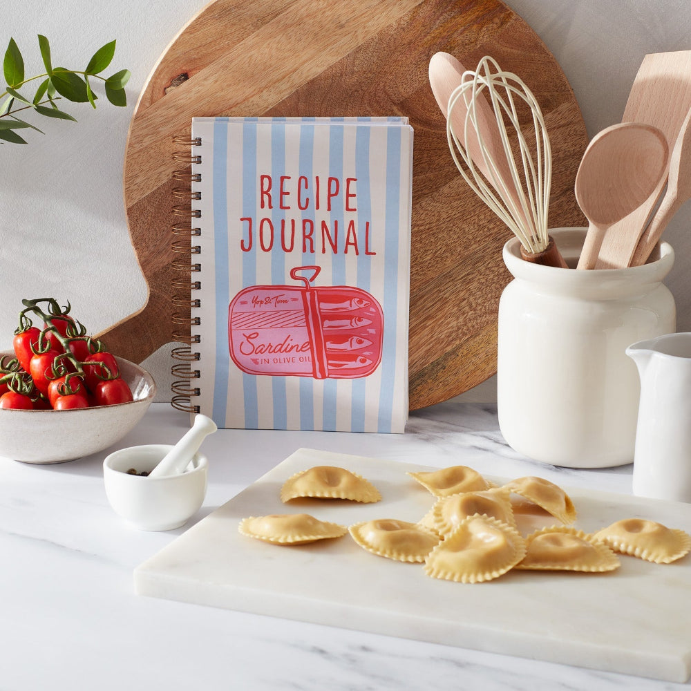Recipe journal with striped cover on a kitchen counter with pasta and utensils