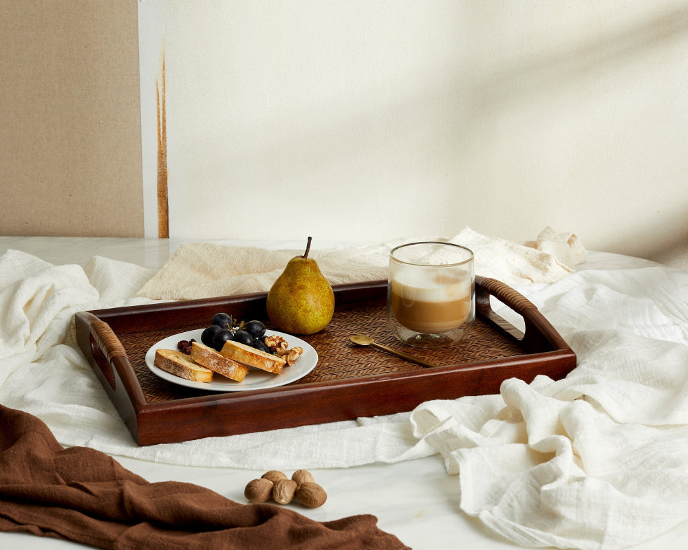 Wooden tray with a plate of food, a glass of coffee, and a pear on a white surface.