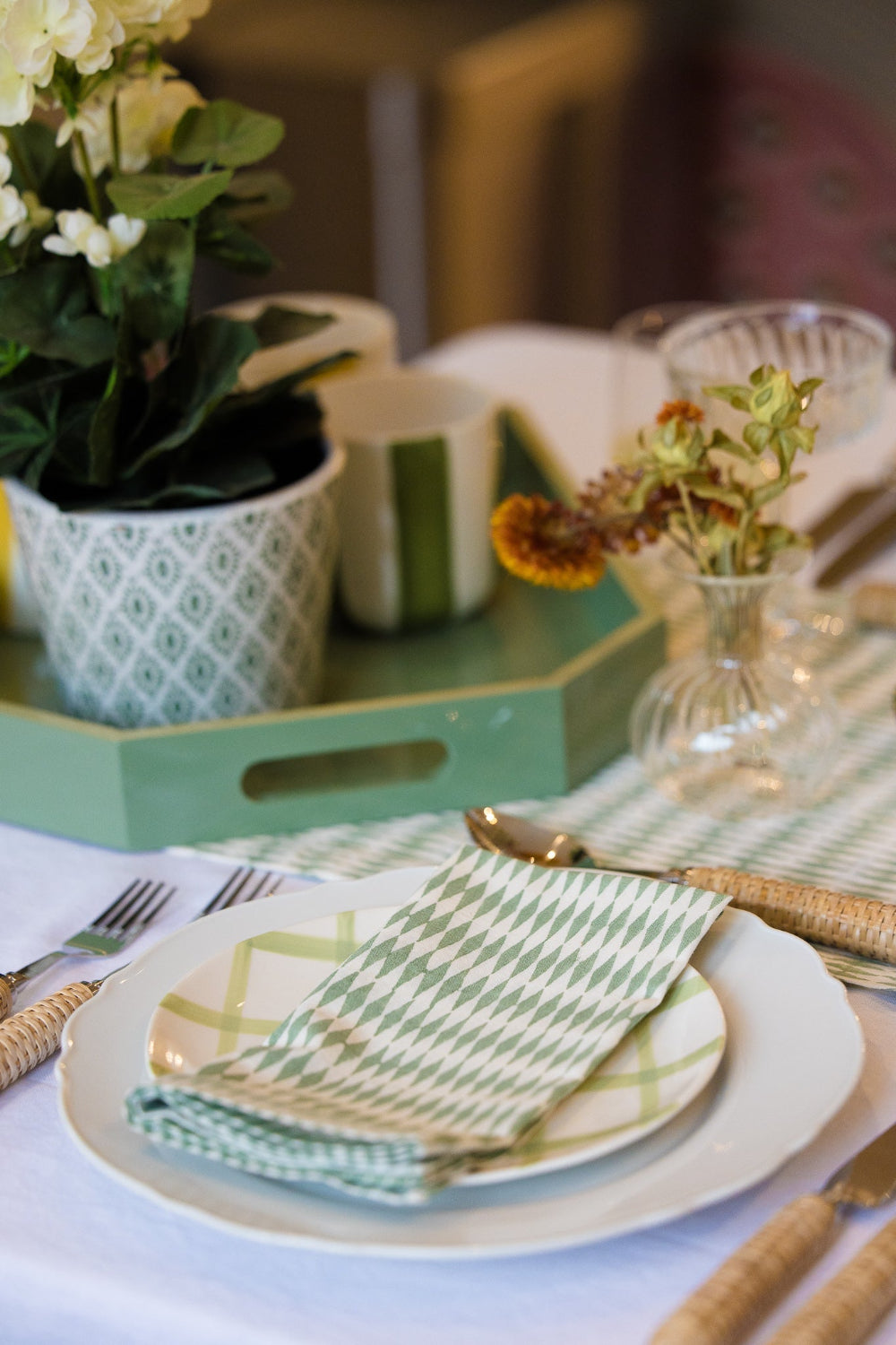 Table setting with green and white plates, napkins, and a vase of flowers.