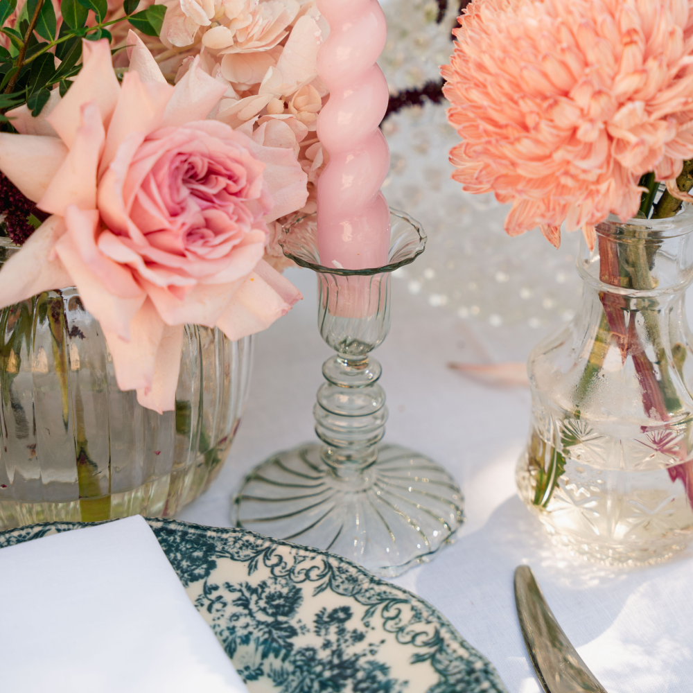 Decorative table setting with pink flowers, candles, and a patterned plate.