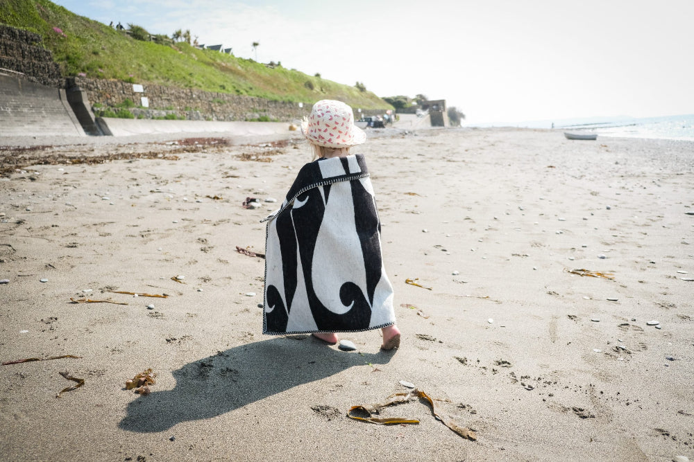 Child wrapped in a black and white patterned towel on a sandy beach