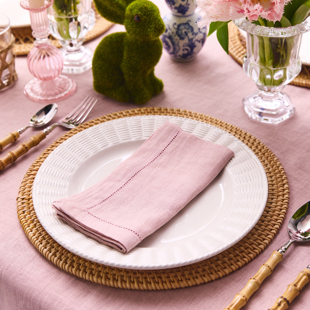 Easter table setting with pink napkin, white plate, and decorative elements on a pink tablecloth.