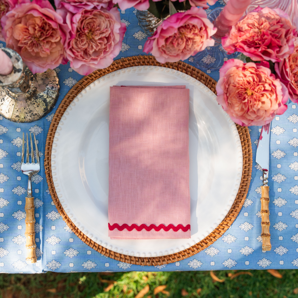 Table setting with pink napkin, white plate, and floral decorations on a blue tablecloth.