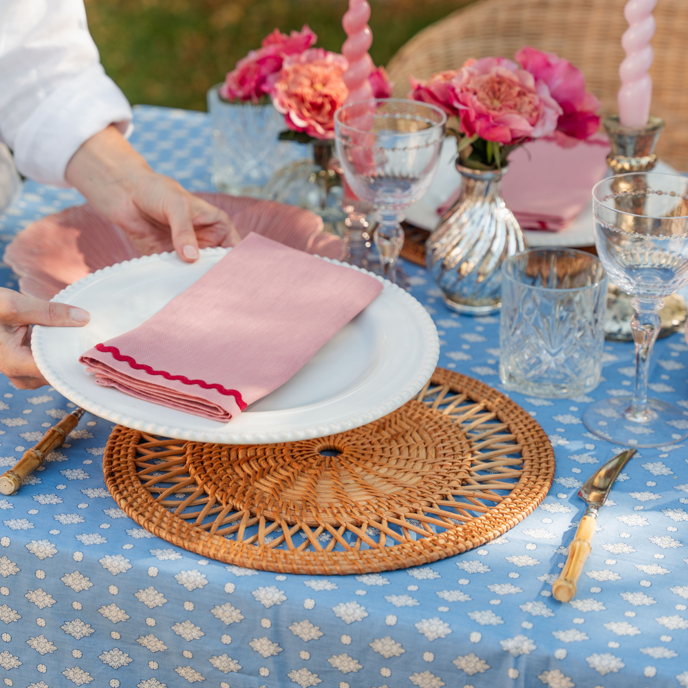 Person setting a table with pink napkins and a blue tablecloth.