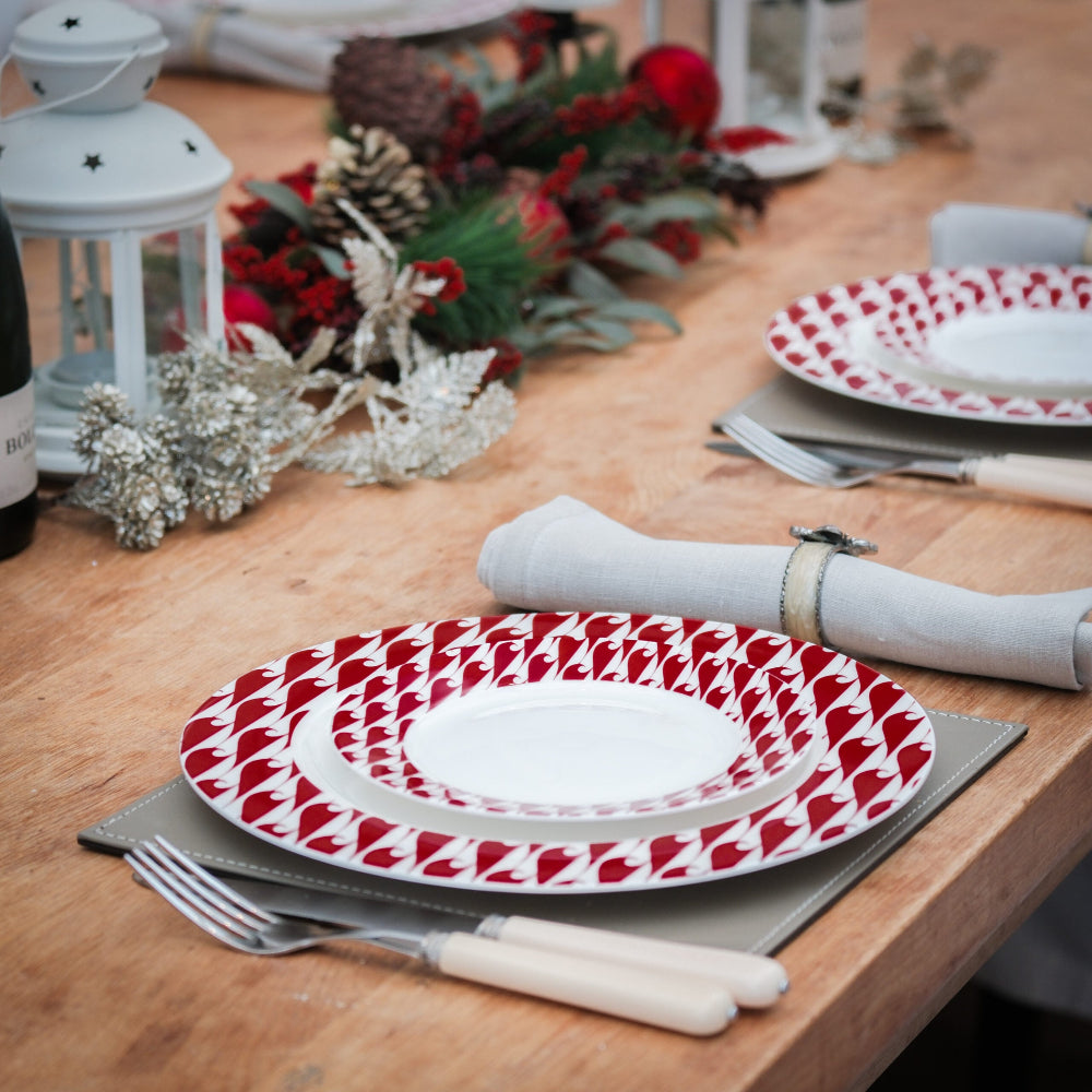 Christmas Table setting with red and white patterned plates, silverware, and decorative items on a wooden table.