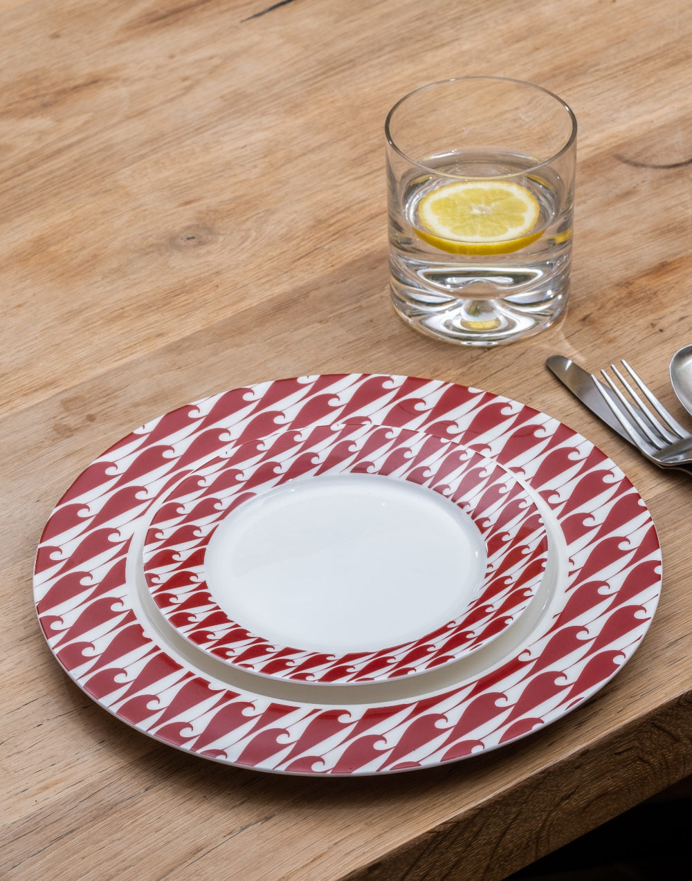 Red and white patterned plate on a wooden table with a glass of water and lemon.