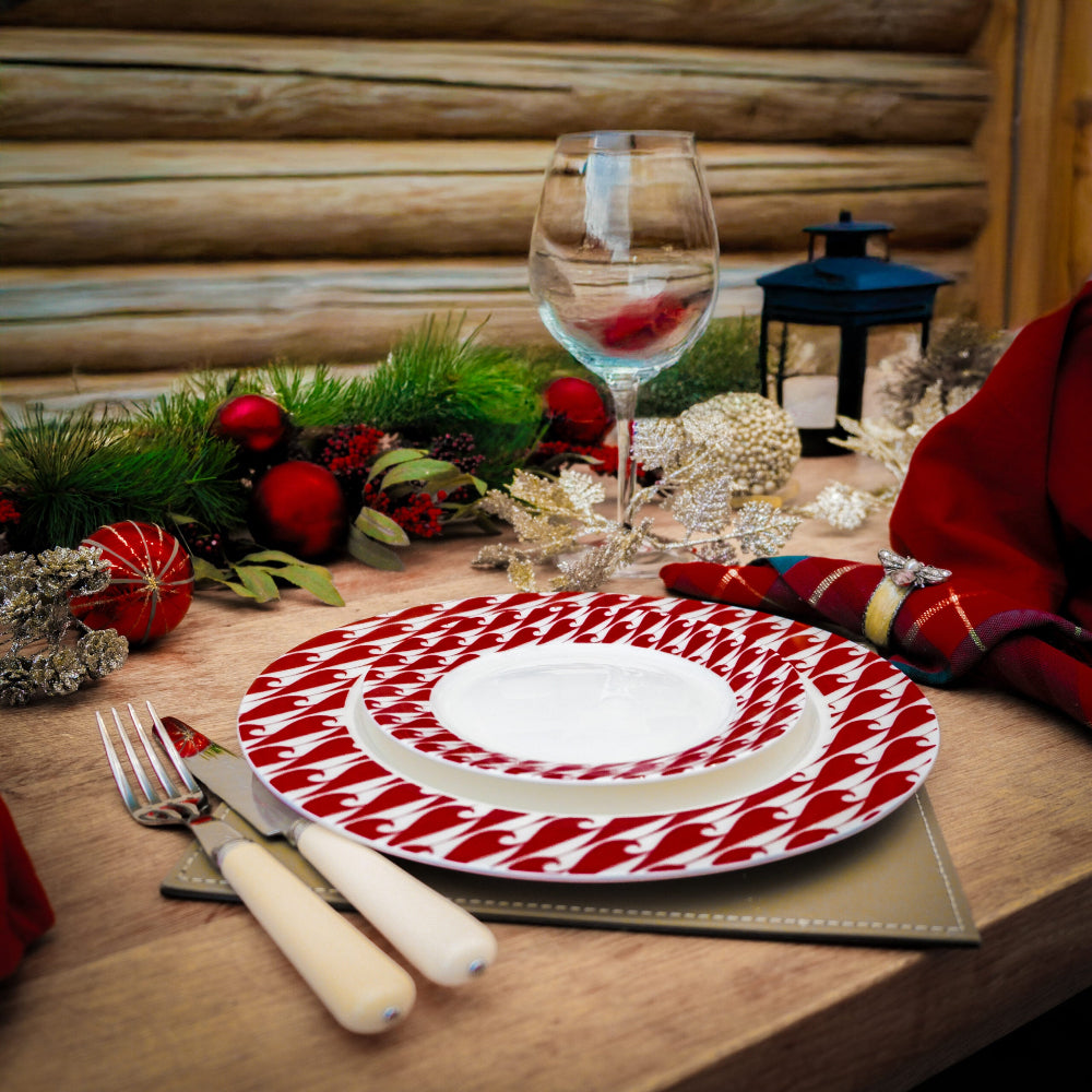 Christmas-themed table setting with a red and white patterned plate, wine glass, and festive decorations.
