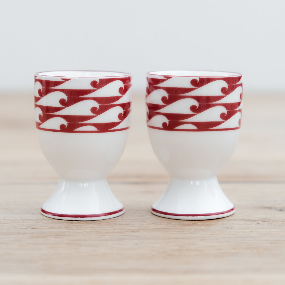 Two ceramic egg cups with red wave pattern on a wooden surface