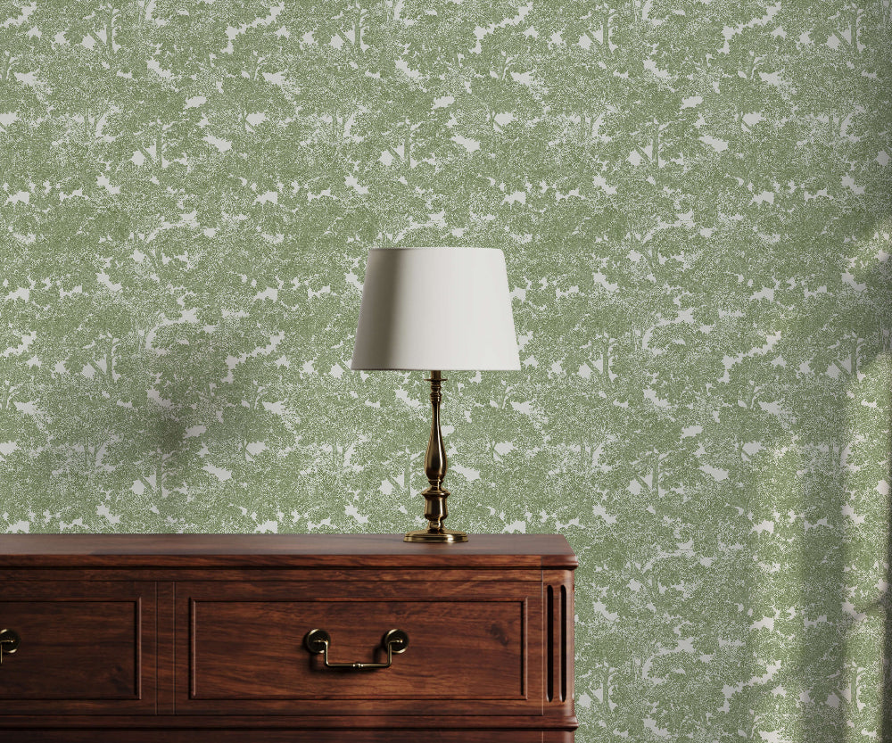 Wooden dresser with a lamp against a green tree patterned wallpaper