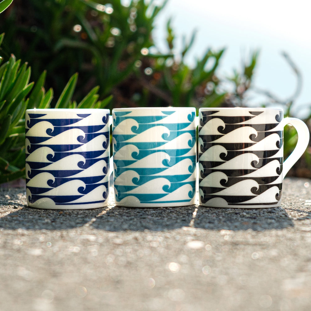 Three ceramic mugs with wave patterns on a concrete surface with greenery in the background