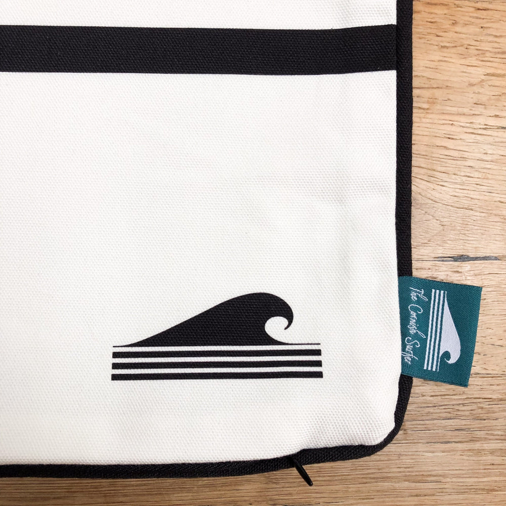 White cushion cover with black wave design and a green tag 'The Cornish Surfer' on a wooden surface