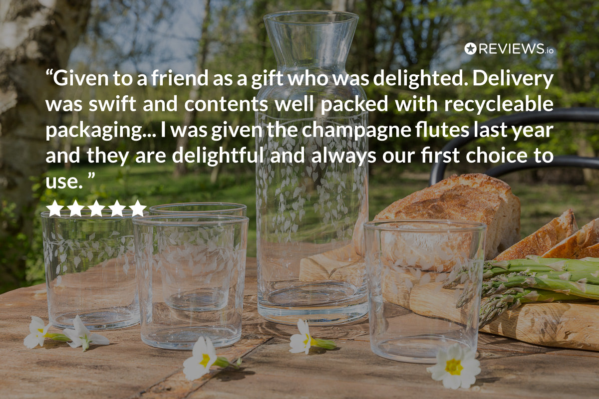 Clear glass flutes on a wooden table with bread and asparagus, surrounded by greenery.
