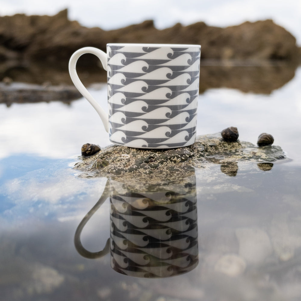 Mug with wave pattern on a beach with water and rocks in the background