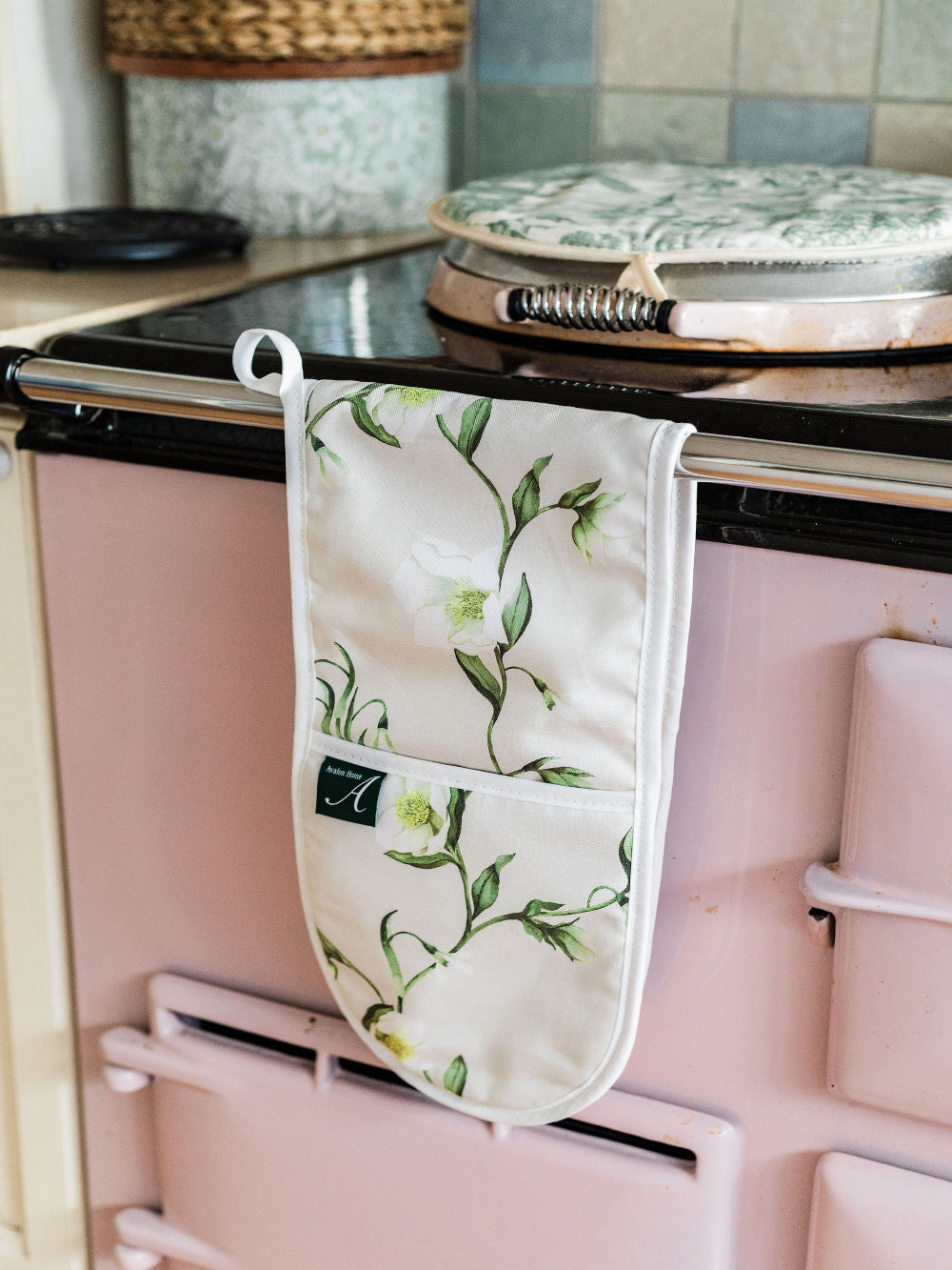 Floral-patterned oven mitt hanging on a pink Aga range cooker.