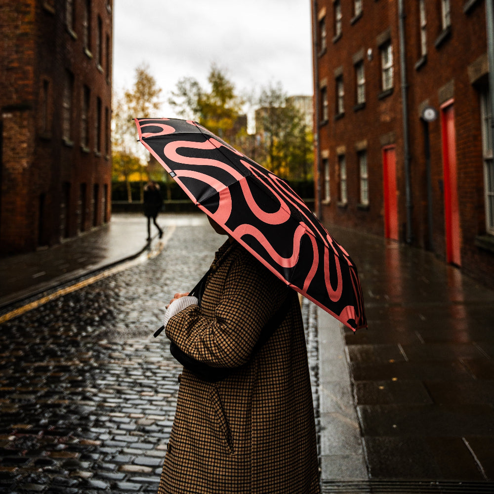 Person holding a black and red umbrella on a rainy street with brick buildings.