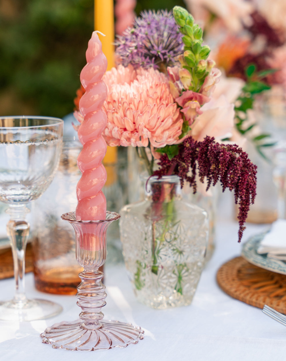 Decorative pink candle in a glass holder on a table with flowers and glasses.