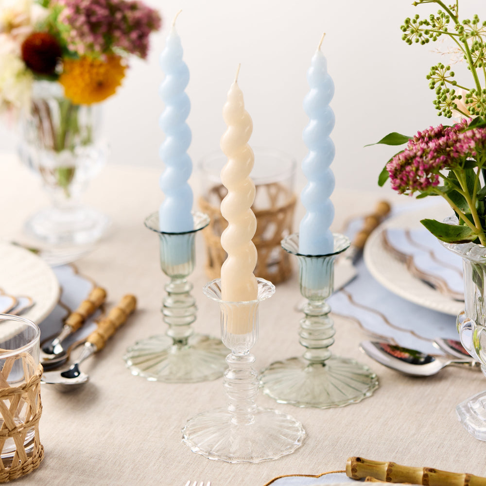 Decorative candles in glass holders on a table with floral arrangements and tableware.