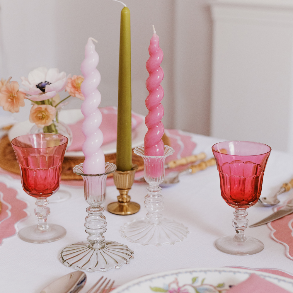 Decorative table setting with pink and green twisted candles, red glasses, and floral tablecloth.